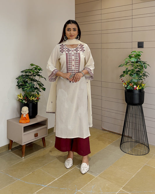 Woman in a white embroidered kurta with maroon pants standing in a modern interior setting.