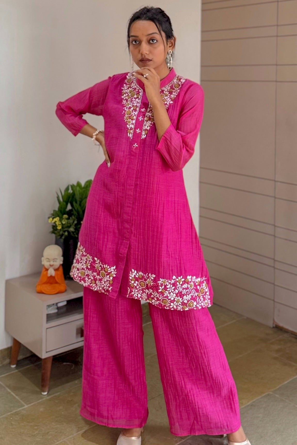 Woman wearing a pink traditional outfit with floral embroidery indoors.