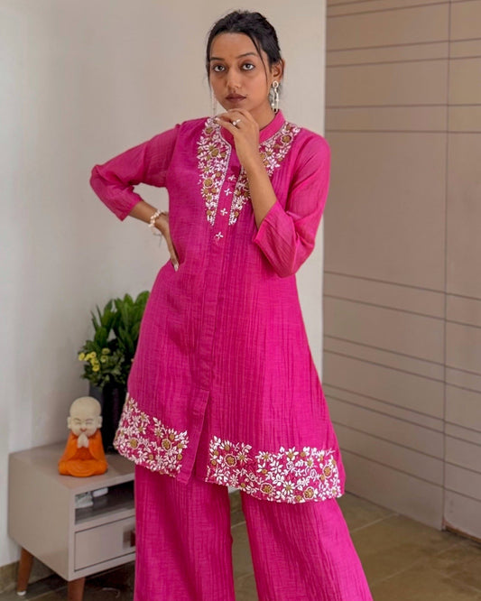 Woman wearing a  pink traditional outfit with floral embroidery indoors.