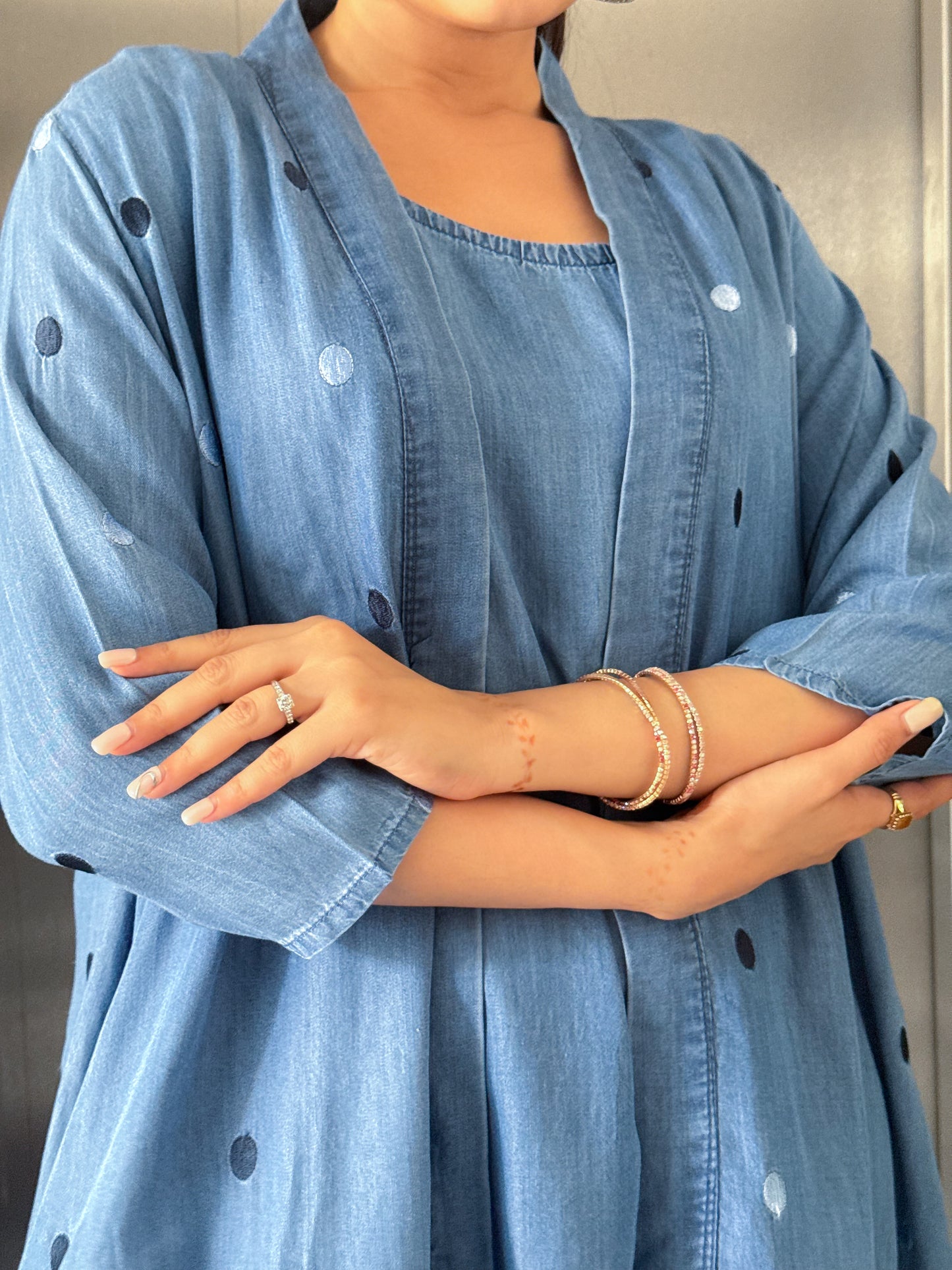 Person wearing a blue denim outfit with arms crossed, showing jewelry.
