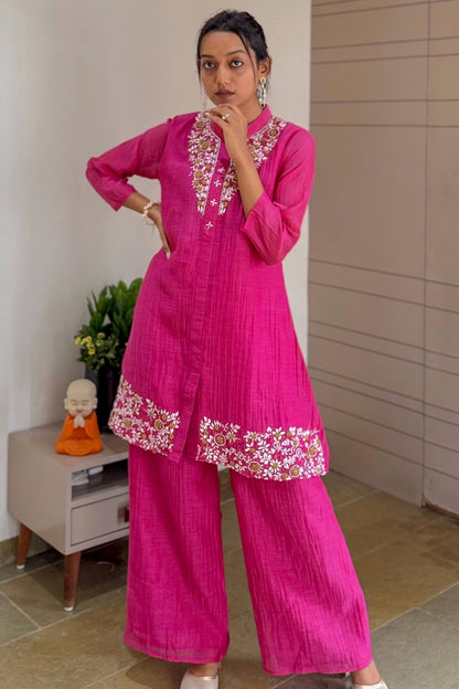 Woman wearing a  pink traditional outfit with floral embroidery indoors.