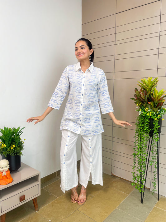 Woman in a white outfit standing in a room with plants and a small table.