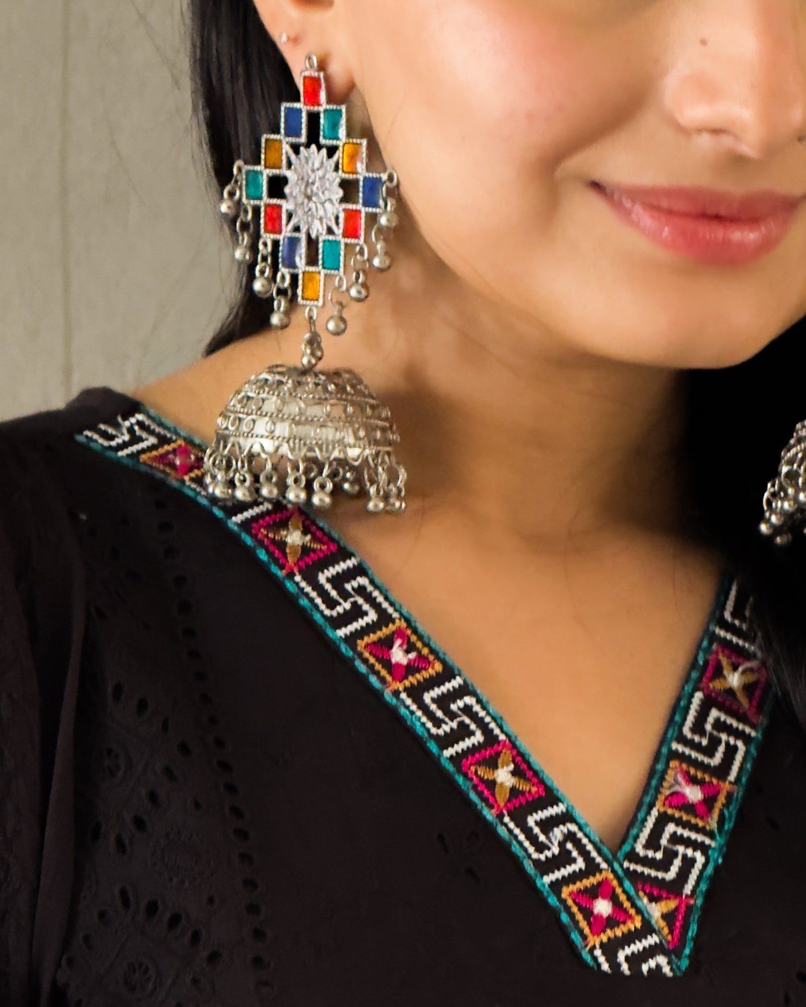 Close-up of a person wearing colorful earrings with a black outfit featuring intricate patterns.