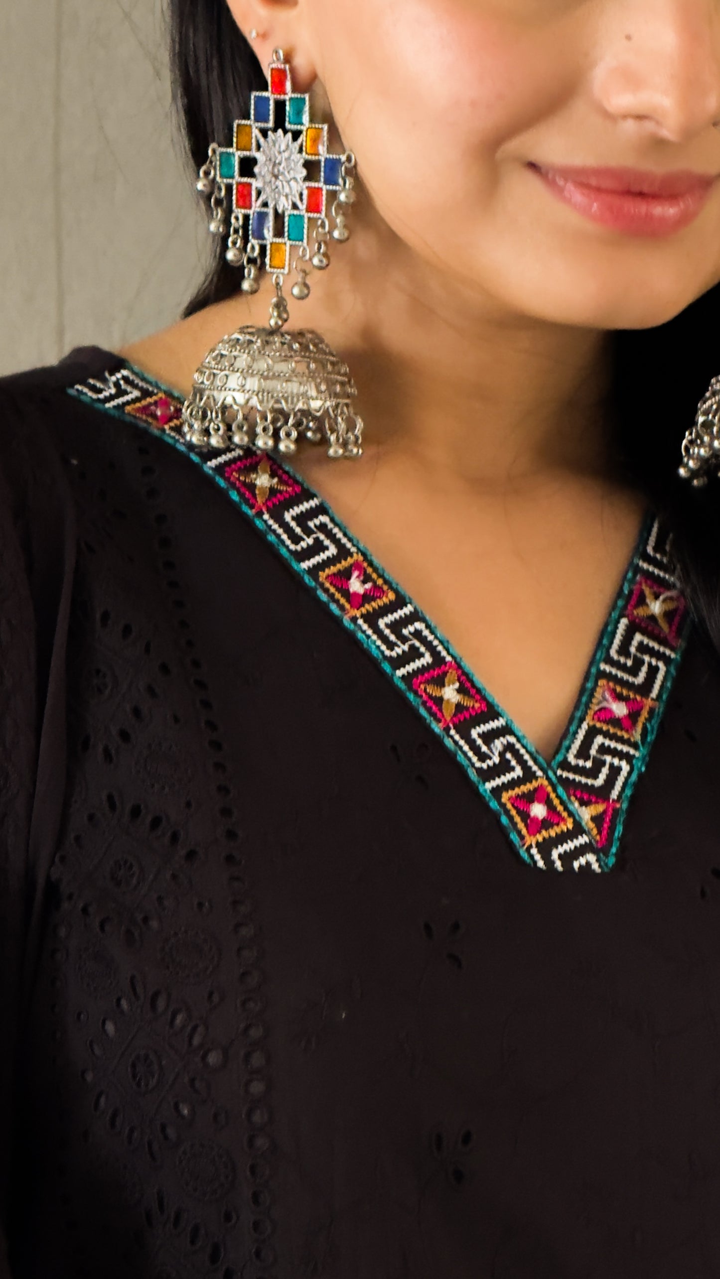 Close-up of a person wearing colorful earrings with a black outfit featuring intricate patterns.