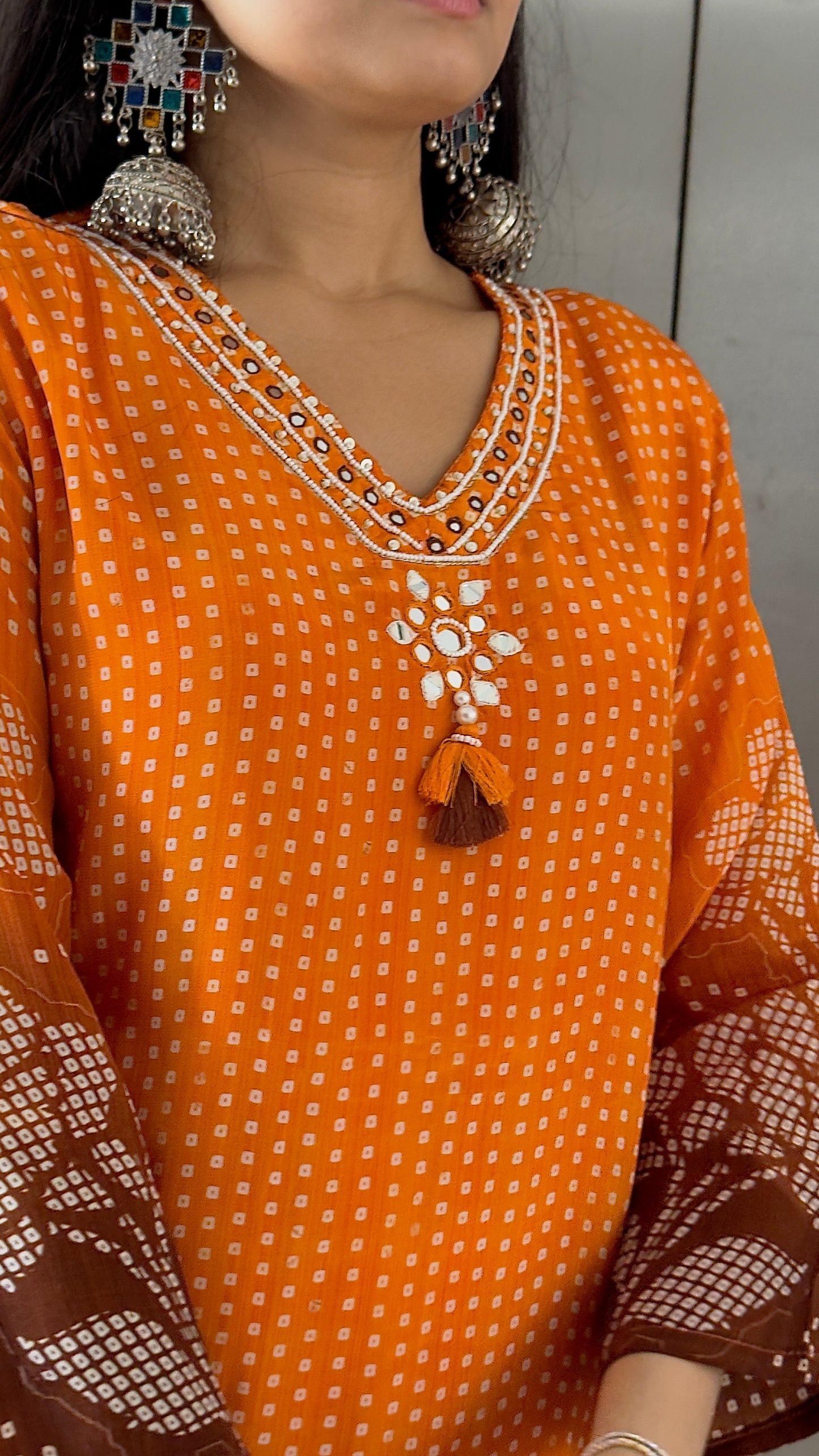 Orange traditional outfit with intricate embroidery and matching earrings.