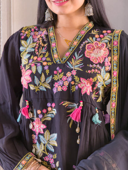 Woman wearing a black embroidered dress with colorful floral patterns.