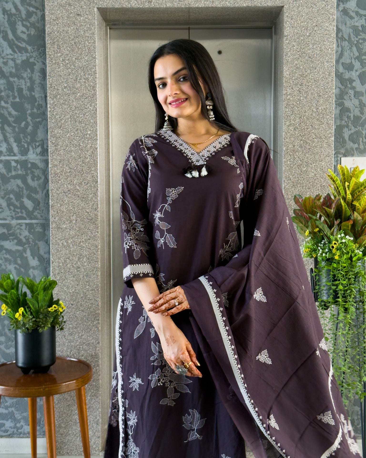 Woman in a dark purple traditional outfit with white patterns standing indoors.