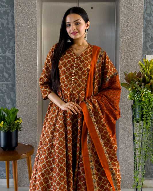 Woman wearing a patterned dress with an orange scarf in a room with plants.