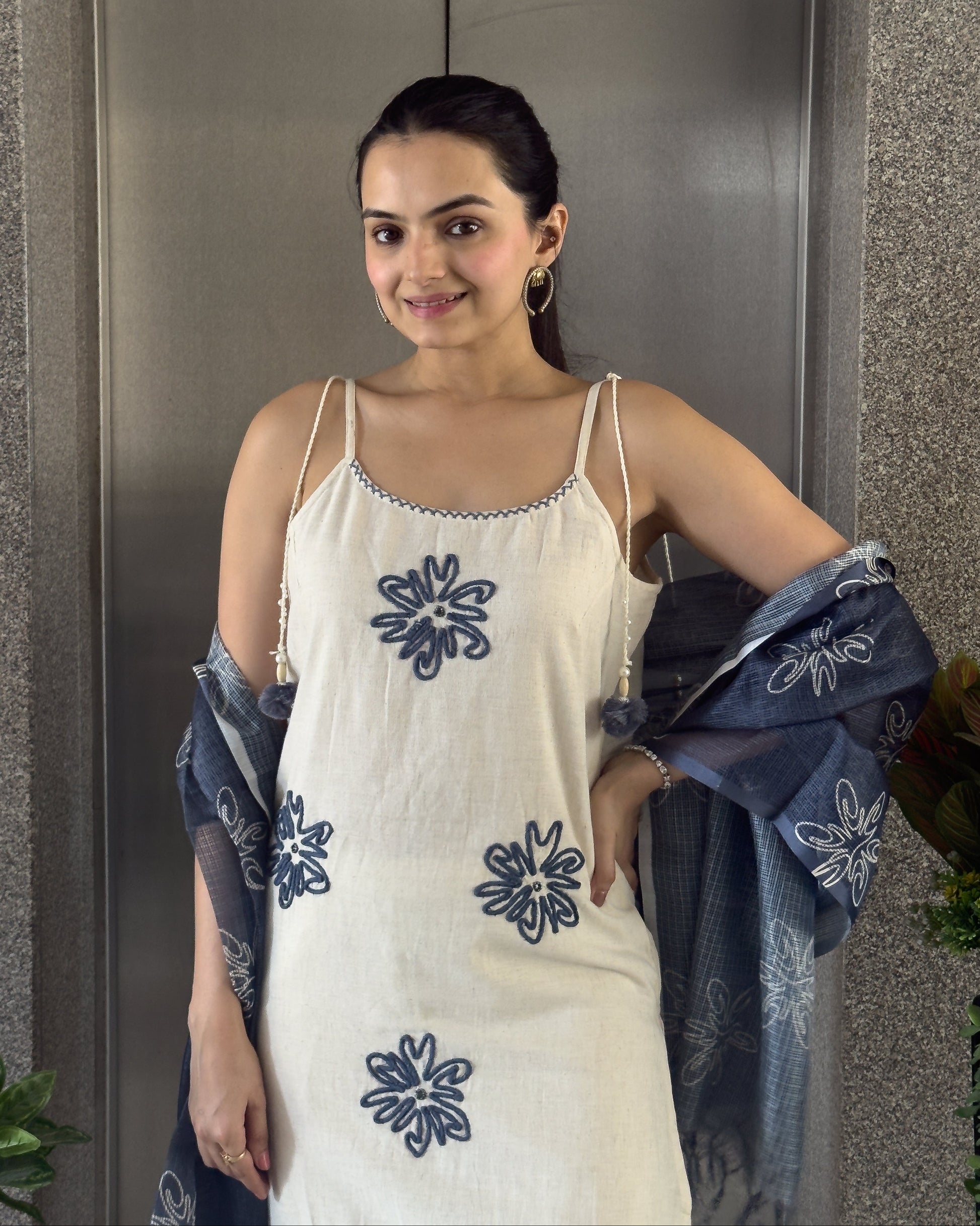 Woman wearing a white dress with blue floral patterns, standing against a neutral background.