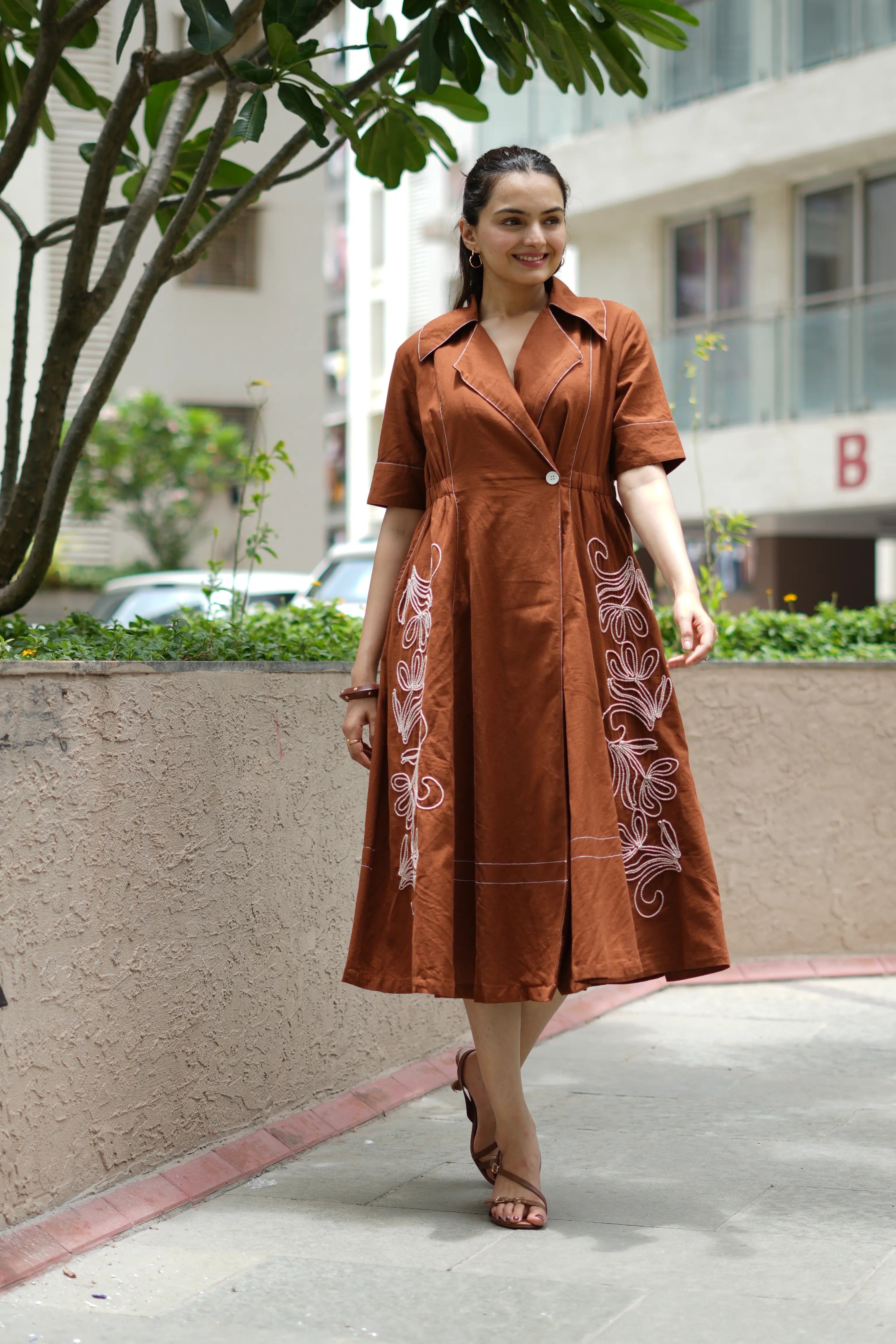 Woman wearing a brown khadi cotton A-line dress with elegant floral embroidery.